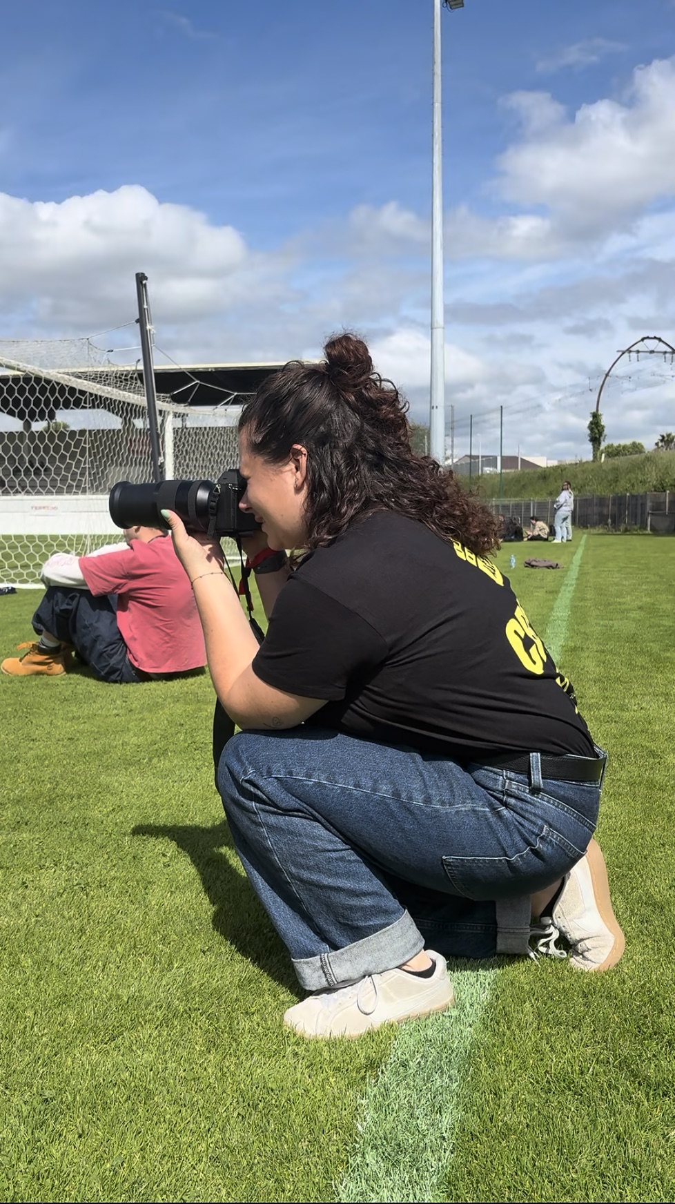 Maëlys accroupie sur un terrain de sport en plein jour, appareil en main