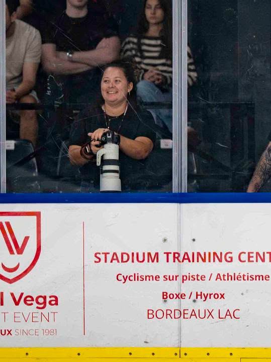 Maëlys souriante, appareil en main, en tribune lors d'un match de hockey sur glace