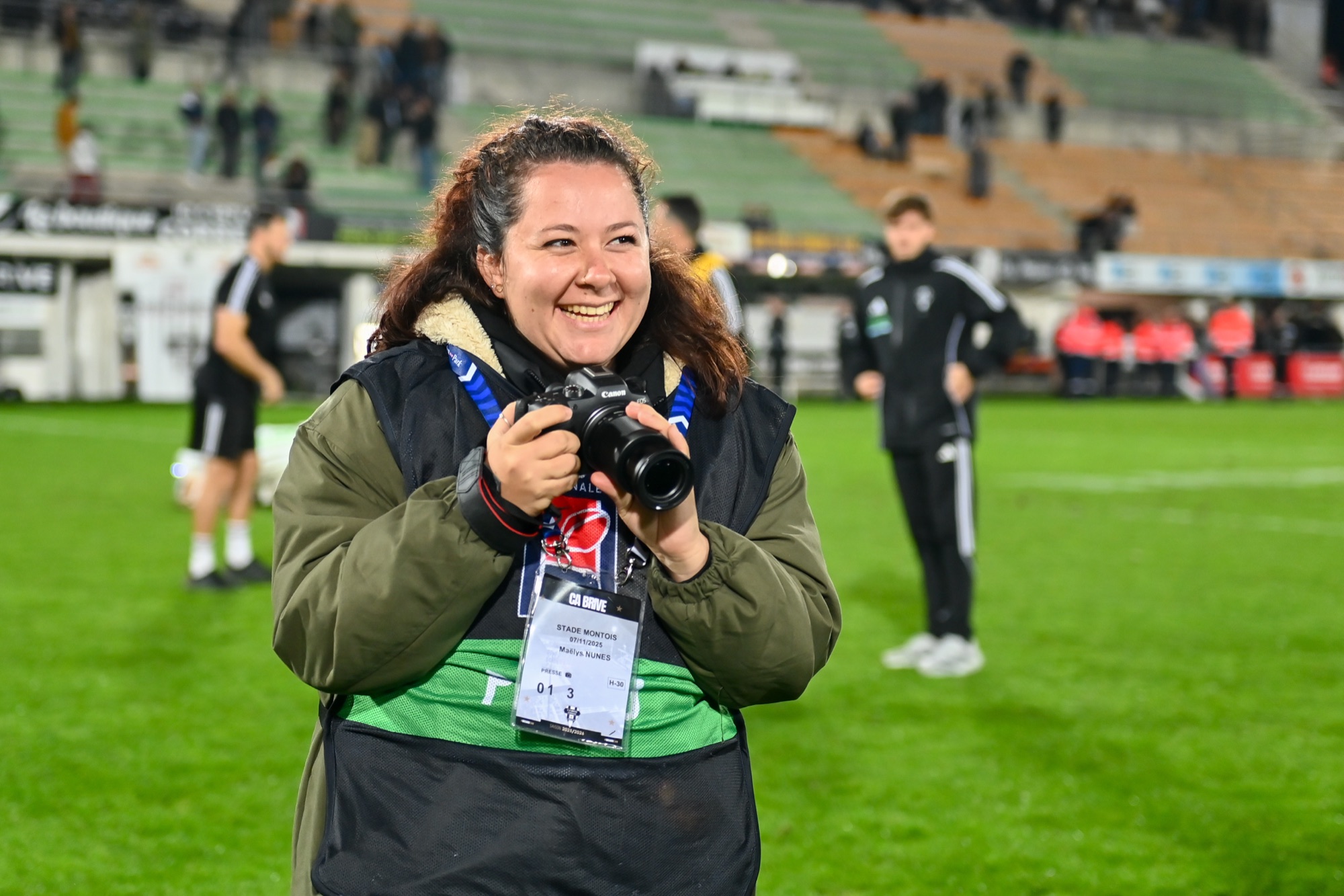 Maëlys souriante, appareil photo en main, au bord d'un terrain de rugby